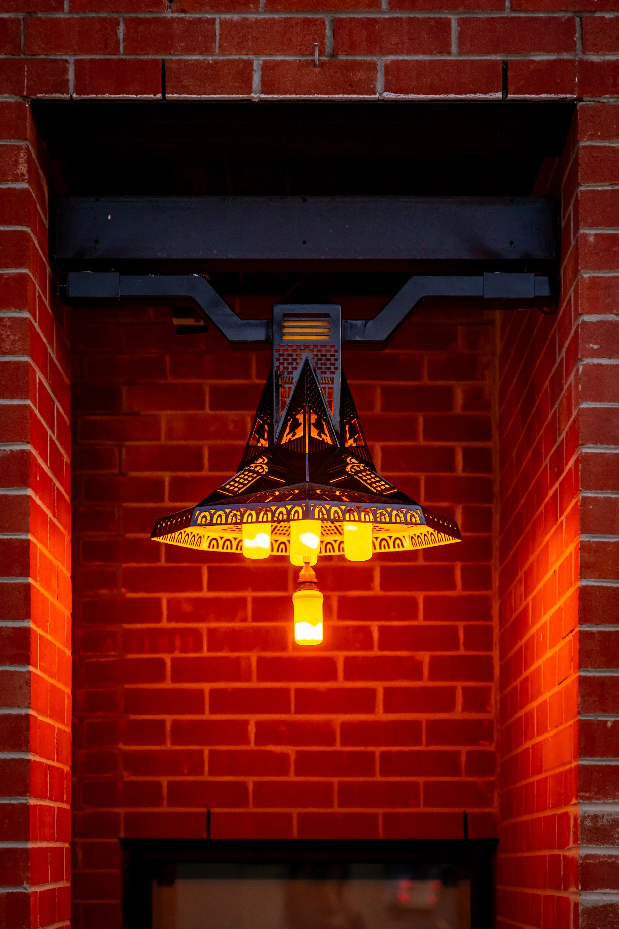 The illuminated Bolton Fire Bell sculpture installed against a brick wall